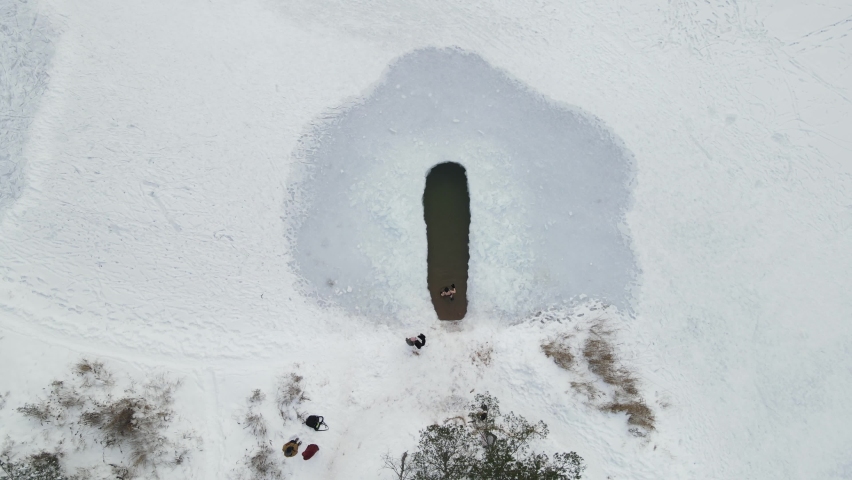 Winter swimming. Woman in frozen lake ice hole. Swimmers wellness in icy water. How to swim in cold water. Beautiful young female in zen meditation. Gray hat and gloves swimming clothes. Nature lake