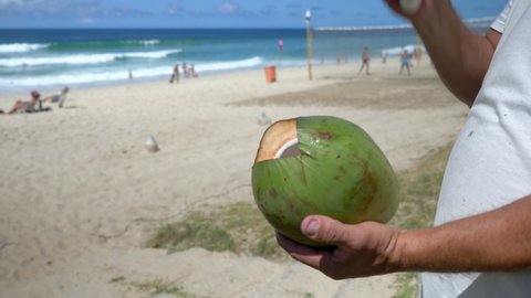 Man holding the chop knife to peeling and shelling a green fresh coconut on the beach in Rio de Janeiro, Brazil
