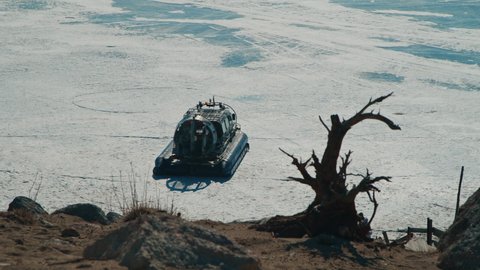 Hovercraft rides on frozen lake ice among snow capped mountains.