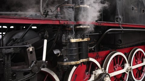 Vintage steam train locomotive, locomotive wheels. High quality. Steam train departs from railway station. Old vintage steam train on the rail road. Smoke covering, wheels