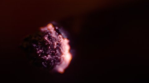MACRO, DOF: Close up view of a cigarette burning as smoker takes a long drag in the darkness. Detailed shot of a burning joint of a person smoking weed at night. Tobacco and rolling paper burning.