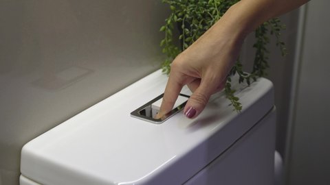 Close up of woman's hand pull toilet seat lid down and press low flush button in modern dual flush system toilet to use less water. Eco friendly lifestyle, water saving, environmental problem concept.