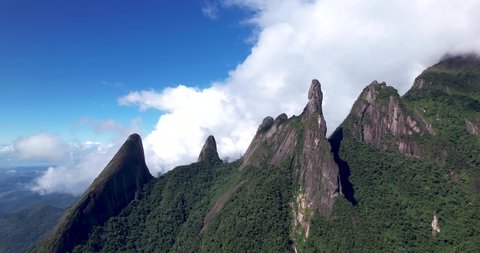 Aerial slow approach in Brazilian panoramic landscape of mountain range Serra dos Orgaos in Teresopolis, Rio de Janeiro with Dedo de Deus, Gods finger, peak in the middle and clouds behind
