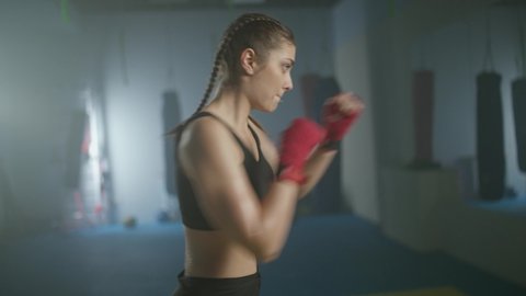 Caucasian female fighter trains his punches and defense in the boxing gym, a boxer trains in front of a mirror, 4k slow motion.