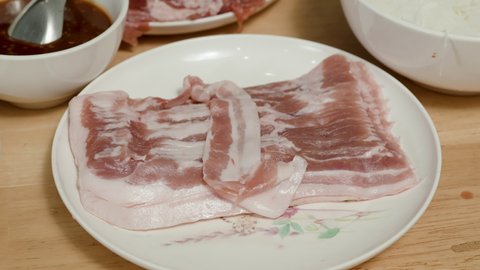 4K, Thinly sliced red pork is placed on a plate to prepare sukiyaki on a table in a restaurant.
