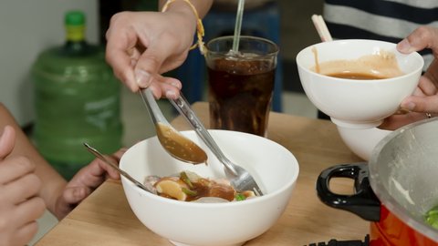 4k, A close-up hand is using a spoon to scoop the dipping sauce into the sukiyaki cup to prepare a delicious meal.
