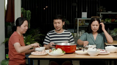4k, A group of 3 Asian friends are eating sukiyaki in a restaurant in front of them with sukiyaki condiments and red sukiyaki pots.
