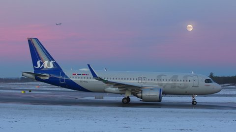 Oslo Airport Norway - December 16 2021: airplane airbus a320 neo taxiing at night very peri pantone sky colors full moon another aircraft passing in air above