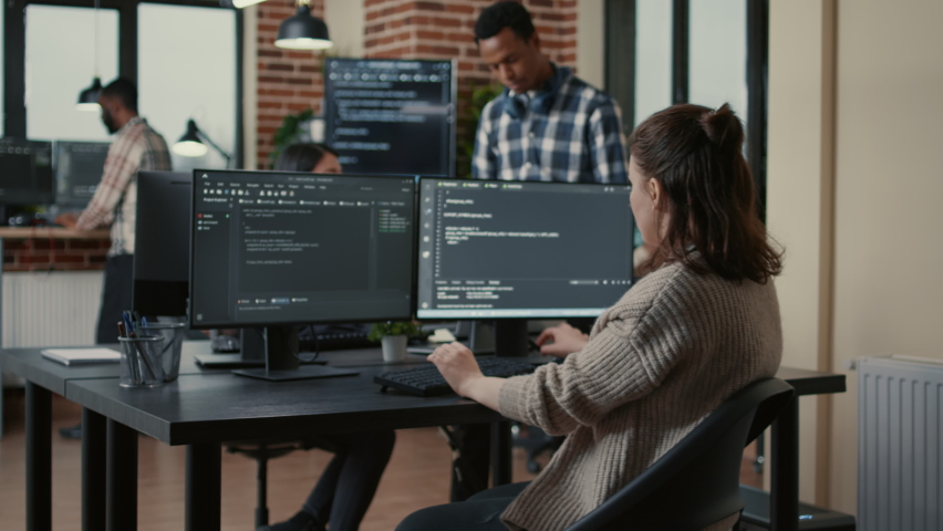 Focused software developer writing code looking at multiple computer screens displaying machine learning algorithm. Programer coding user interface while colleagues doing teamwork in background. Royalty-Free Stock Footage #1085102045