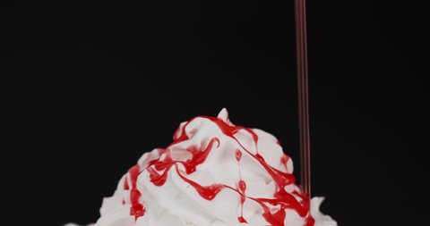 Pouring strawberry sauce on top whipped cream. Soft whipped cream on black background.