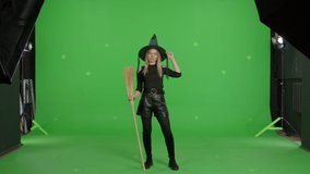 Young caucasian woman wearing witch hat for halloween parties over green screen background. Girl having fun with a broom making like playing the guitar . Halloween concepte. Chroma key. 4k video