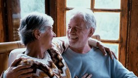 Young senior happy couple sitting together on a bamboo chair at home in wooden chalet enjoying winter or autumn season with love and friendship. Old mature people lifestyle - Powered by Shutterstock - Get 15% off with code: PIKWIZARD15