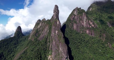 Aerial slow panning panorama landscape of mountain range Serra dos Orgaos in Teresopolis, Rio de Janeiro, Brazil, with God's finger peak in the middle and clouds behind