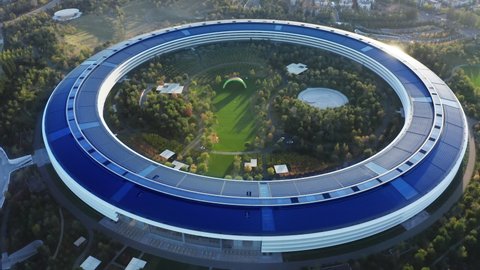 Apple Campus, Cupertino, Palo Alto, Silicone Valley 2022 California USA. Cinematic aerial view of modern futuristic building landmark named spaceship with green park and rainbow arch at golden sunset