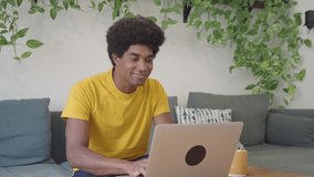 Young African American man working remotely in an apartment with a laptop. 