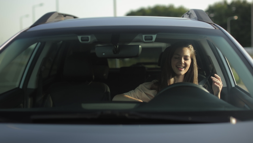 A happy woman is sitting in her car in the driver's seat. She is listening to music and dancing. She is smiling. 4K Royalty-Free Stock Footage #1085112965