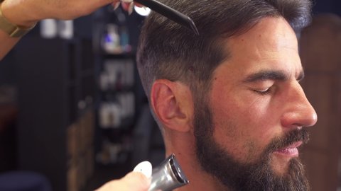 Male haircut with electric razor. Close up of man hair cut. Female hands barber shaving man with electric razor in barbershop. Barber cutting hair with hair trimmer. High quality 4k footage