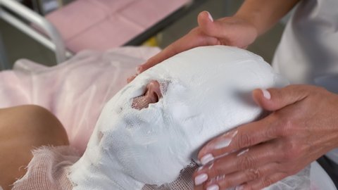 Professional beautician is covering woman's face with foam mask and gauze in cosmetology clinic. Cosmetologist doctor is making beauty procedure against facial wrinkles. Anti-aging effect.