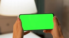 Girl's Hands Hold Horizontally Mobile Phone with Green Screen, Green Background, Mockup, Chroma key, Close-up. Video Communication, Advertising Product, Internet Search, Social Network Browsing.