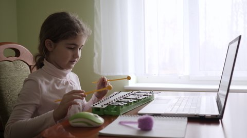Distance Learning. Schoolgirl Studying Online Using Laptop Music Lesson. School Student Wearing Headphones Watching Internet Video Music Course. Caucasian Girl Learning to Play Xylophone, Piano.