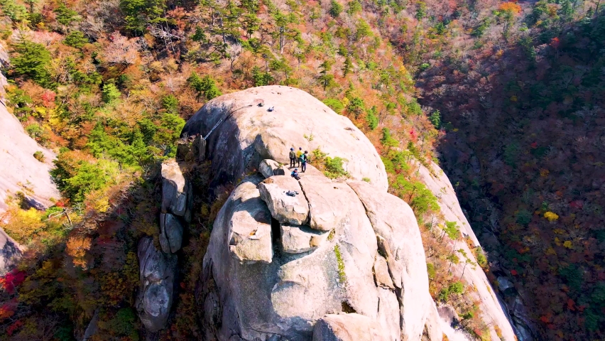 Men standing on a rock surrounded by red, yellow and green autumn leaves in a mountain climbing forest