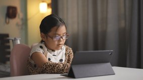 Asian child wearing blue block eyeglasses for learning on computer tablet and touch screen or kid girl student smile to video call and studying online class or person learn from home school in bedroom