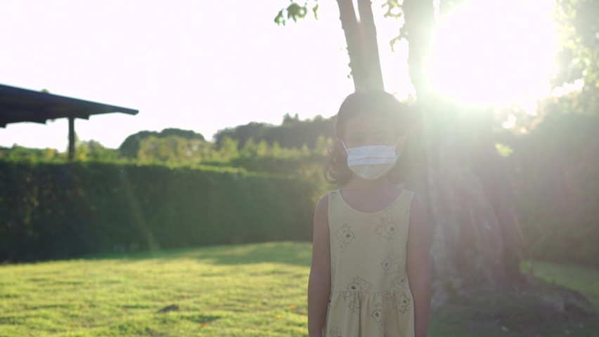 Small girl with protective face mask walking on field at dusk.