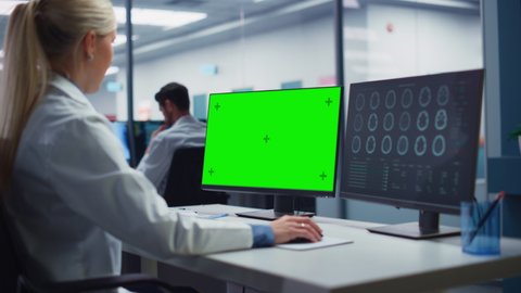 Hospital Research Lab: Female Medical Biotechnology Scientist Working on Green Screen Chroma Key Computer with Brain Scan MRI Images. Professional Neurologist Analysing CT Scan. Over Shoulder