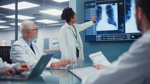 Hospital Conference Meeting Room: Black Female Physician Presents Patient X-ray on TV Screen, Team of Medical Doctors Discuss Treatment. Research Scientists Talk of Cure, Drug, Medicine Development