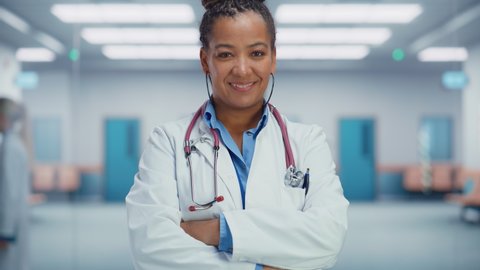 Medical Hospital Medium Portrait: Confident African American Female Medical Doctor Crosses Hands, Looks at Camera and Smiles. Professional Black Physician in White Lab Coat Ready to Save Lives