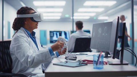 Futuristic Medical Hospital: Black Female Neurosurgeon Wearing Virtual Reality Headset Uses Controllers to Remotely Operate Patient with Medical robot. MRI Image Show Treatment of Neurological Disease