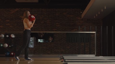 Alone Caucasian blonde woman throws a bowling ball and knocks out a shoot with one throw dances rejoices and jumps with happiness