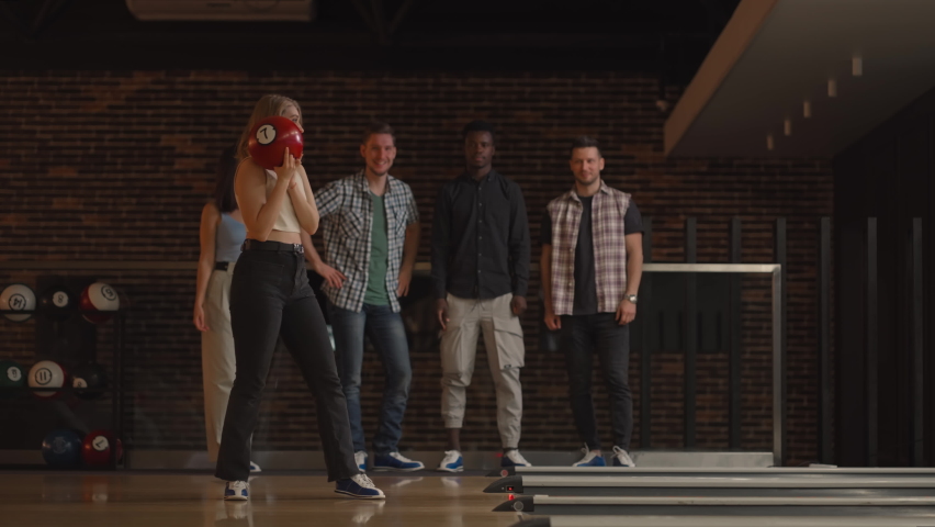 A young blonde woman makes the final throw with a bowling ball and wins the game with the support and joy of her friends of different nationalities. Rejoice and celebrate the victory