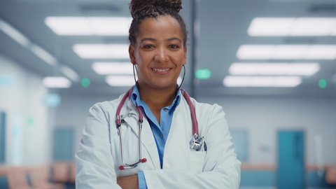 Medical Hospital Medium Portrait: Friendly African American Female Medical Doctor Crosses Hands, Looks at Camera and Smiles. Successful Black Health Care Physician in White Lab Coat