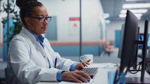 Hospital Laboratory: Black Female Medical Doctor is Working on Computer Analysing Chest, Bones X-rays on Screen. Professional African American Physician Doing Health Care Treatment Research