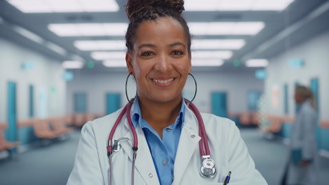 Close Up Portrait of African American Female Medical Doctor with Stethoscope Standing in Hospital Hallway. Successful Black Physician in White Lab Coat Looks at the Camera, Smiles. Ready to Save Lives