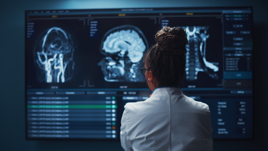Medical Hospital Research Lab: Black Female Neuroscientist Looking at TV Screen, Analyzing Brain Scan MRI Images, Finding Treatment for Patient. Health Care Neurologist Curing People. Back View Zoom