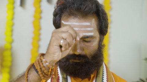 Rack focus, head shot of indian holy guru praying god by holding cowrie shells by chanting hymns at monastery - concept of astrologer, indian culture and fortune teller.