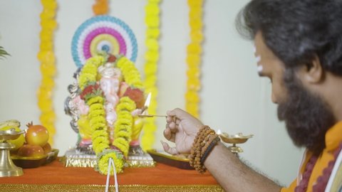 Focus on hand Holy god man or Indian priest offering aarti by chanting hymns in front of lord ganesh idol during festival celebration at home - concept of treditional festival and indian culture.