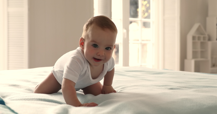 Adorable sweet baby girl or boy crawling on bed smile look at camera, pose inside cozy warm bedroom alone, close up. Cheerful healthy infant portrait, carefree babyhood and childcare, growth concept Royalty-Free Stock Footage #1085132291