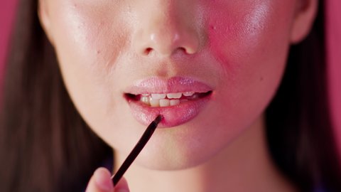 Closeup Shot Of Young Woman Applying Lip Gloss With Makeup Brush, Unedited Footage Of Unrecognizable Female Doing Makeup While Standing Over Pink Background, Using Volumizing Lip Balm, Slow Motion