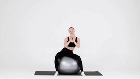 Sporty Millennial Woman Exercising With Fitball Over White Background In Studio, Rotating Her Hips While Sitting On Big Swiss Ball, Fit Young Female Training Pelvic Floor Muscles, Slow Motion Footage