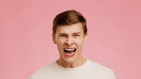 Emotional Guy Shouting And Yelling Looking At Camera Standing Posing Over Pink Background In Studio. Portrait Of Screaming Millennial Man. Omg News Concept. Slow Motion