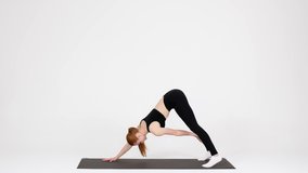 Sporty Young Female Training In Studio Making Downward Facing Dog Exercise And Reaching Toes With Hands, Athletic Lady Streightening Body Muscles While Working Out Over White Background, Slow Motion