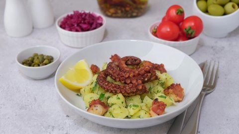 Warm salad with octopus, potatoes, tomatoes, red cabbage, olives, capers and lemon on a white plate. Traditional greek dish. Close-up, white background, zoom in.