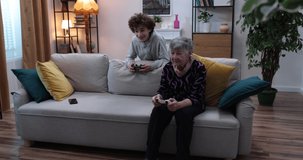 Boy and  senior women playing video game on console. Grandmother and grandson playing video games using gamepads at home. 