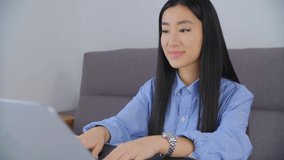 Beautiful young asian woman working on laptop computer in 4k stock footage. Cute Vietnamese girl in 20s doing distant freelance work on notebook pc at home. BIPOC person lifestyle video clip