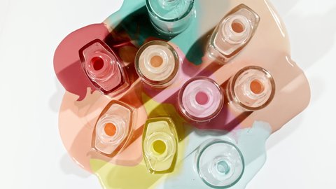 Multicolored nail polish samples spilled on white background isolated. Opened bottles nail varnish, pattern. Fashion, style. Cosmetic products.Top view. Stop motion