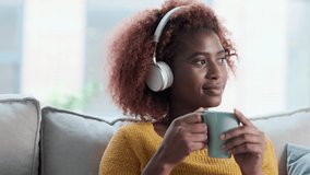 Video of beautiful woman listening to music while drinking a cup of coffee sitting on sofa at home.