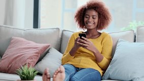 Video of confident young woman using her mobile phone while sitting on sofa at home.